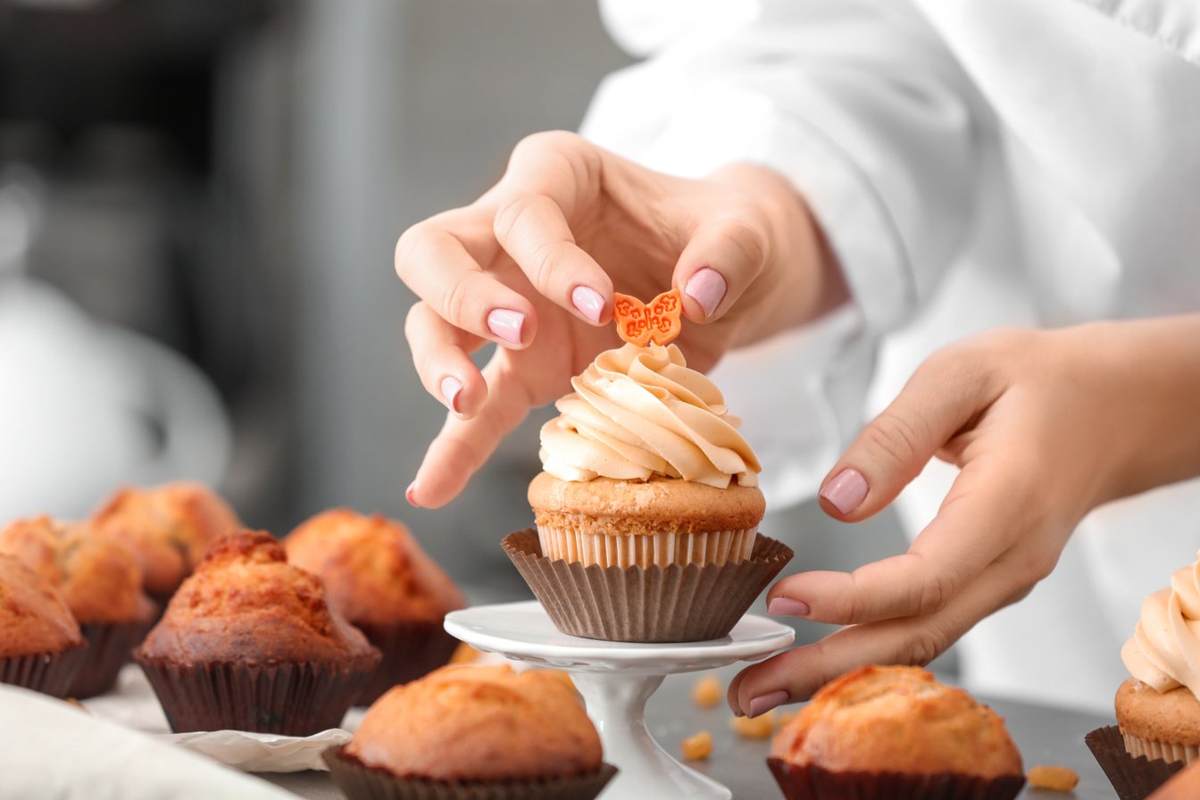 Female Pastry Chef Decorating Tasty Cupcake at Table